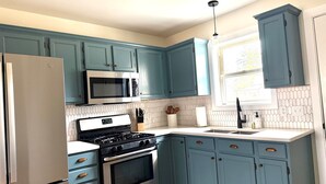 Una cocina con gabinetes color turquesa, un refrigerador de acero inoxidable, un microondas, una estufa y un lavamanos.
