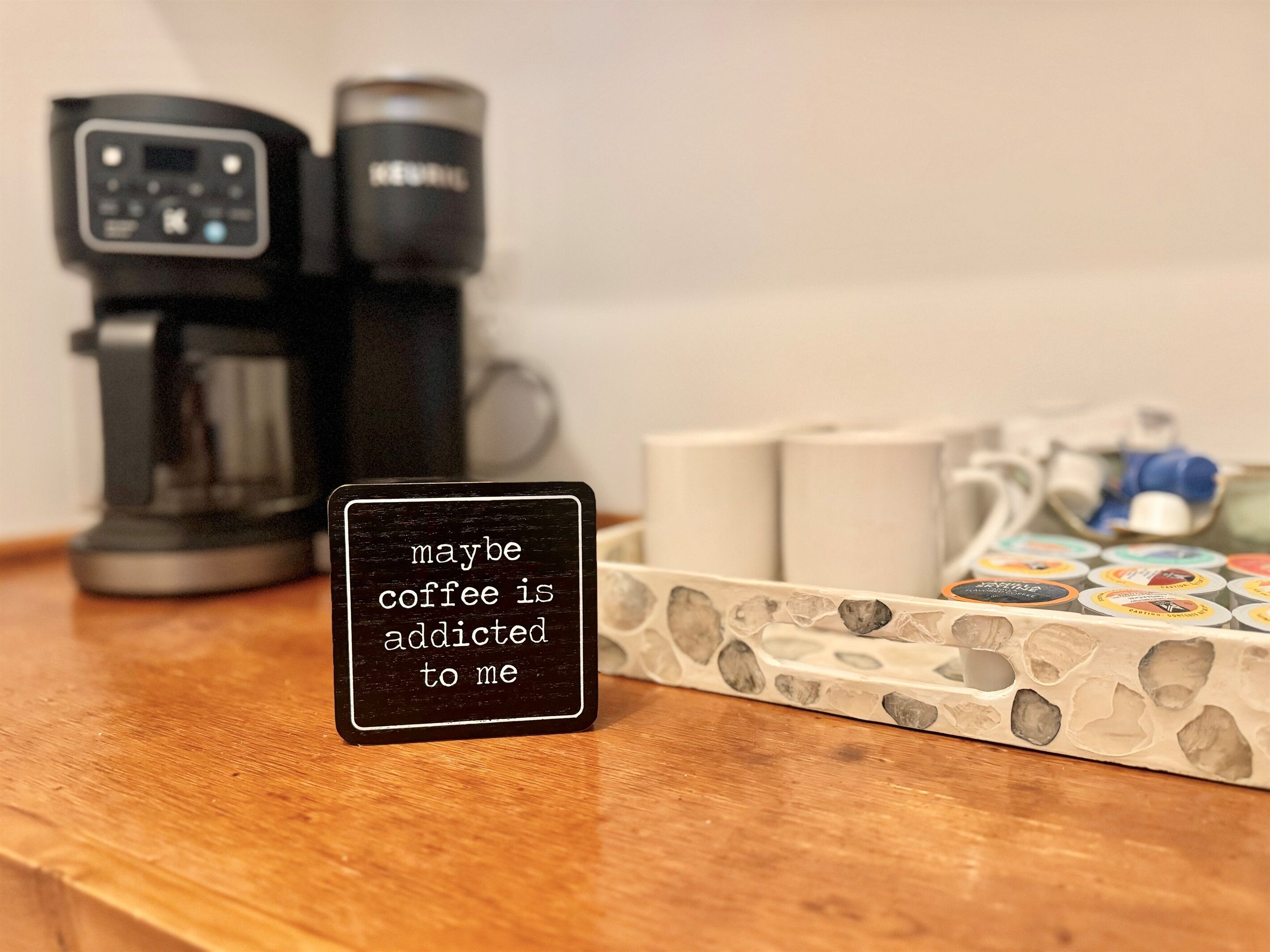 A coffee maker, a coffee pod holder, and a sign with a coffee-related message.