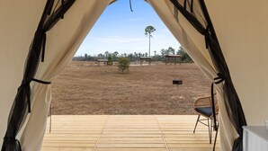 A tented area with a view of a grassy field, a chair, and a small structure in the distance.