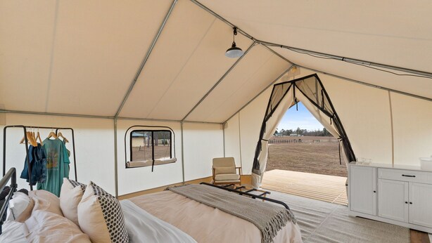 A tented room with a bed, a chair, a wardrobe, a window, and a view of the outdoors.
