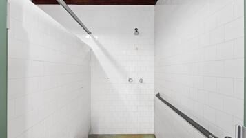 Un box de ducha estrecho, con azulejos, una barra de apoyo y un cabezal de ducha.
