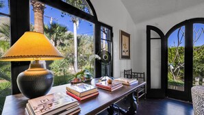 Une pièce avec une grande fenêtre, une table avec des livres, une lampe et une chaise.