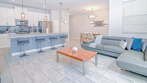Une cuisine moderne avec des tabourets de bar, une table basse en bois et un canapé gris dans l’espace salon.