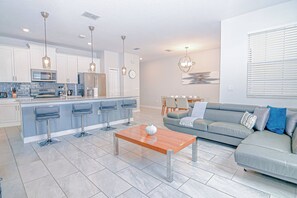 A modern kitchen with bar stools, a wooden coffee table, and a grey sofa in a living area. - Go!#23 - CHAMPIONS GATE (Davenport)