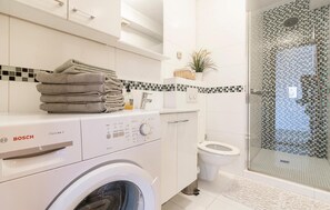 Une salle de bain moderne équipée d’un lave-linge Bosch, de toilettes et d’une douche à parois de verre.
