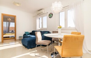 Ein modernes Wohnzimmer mit einem blauen Sofa, einem runden Esstisch und einem gelben Sessel.