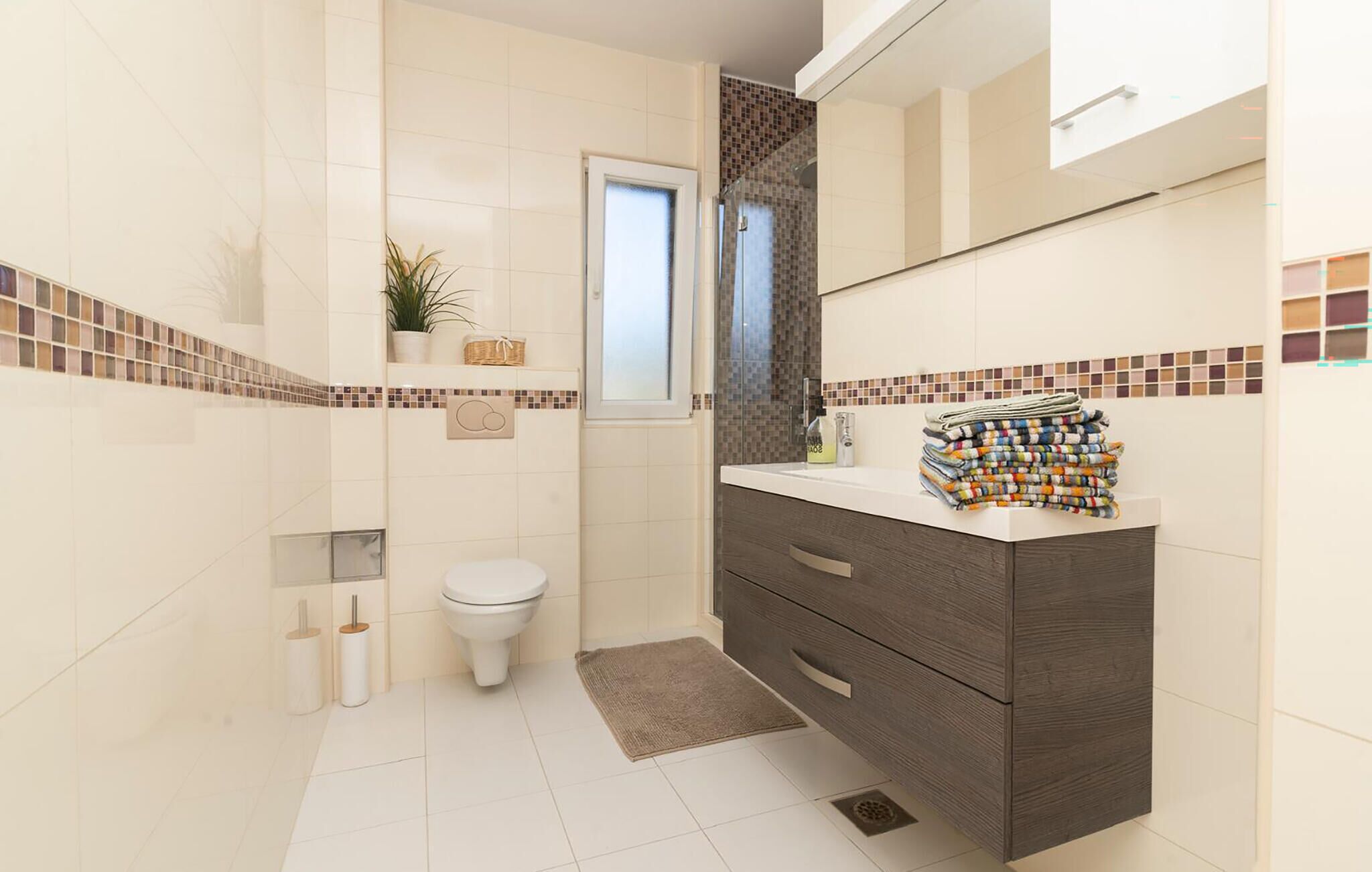 Un baño con inodoro, lavamanos con una pila de toallas y zona de ducha.