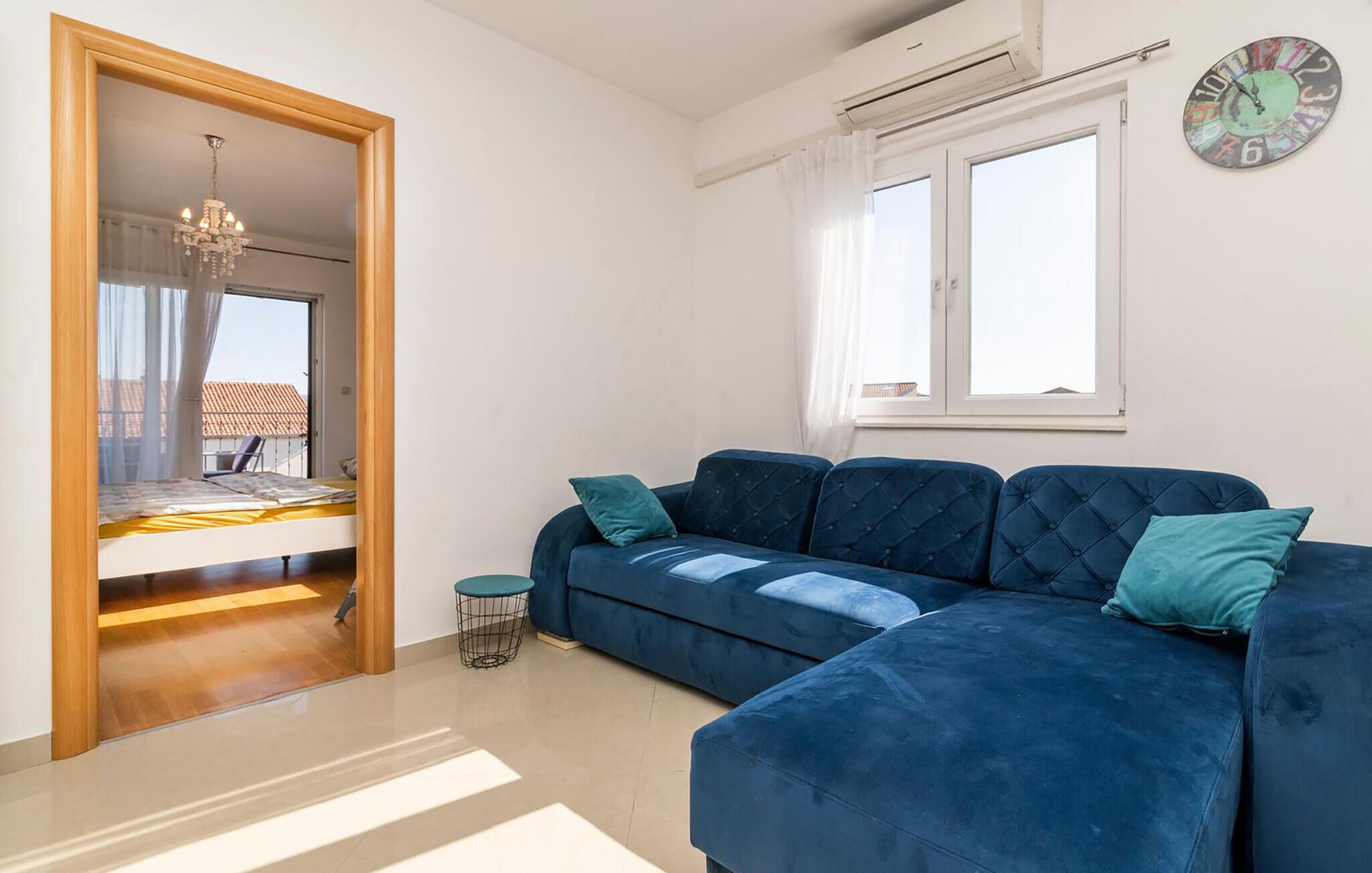 A room with a blue sofa, a small round table, a chandelier, and a clock on the wall.