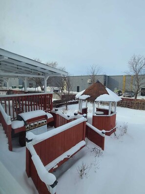 Ein überdachter Außenbereich mit Grill, einer Laube und einem mit Schnee bedeckten Deck.