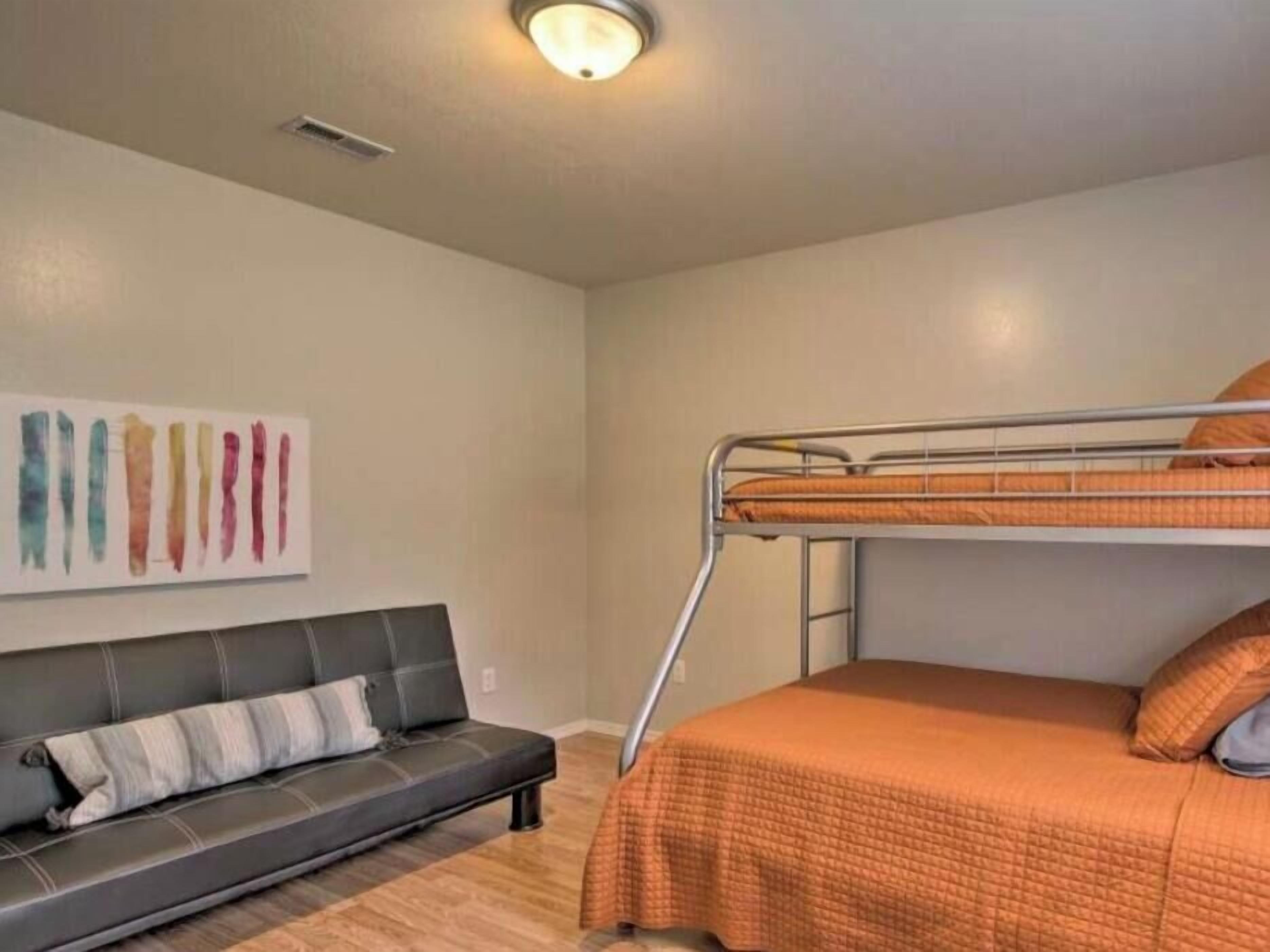 A room with a bunk bed, a sofa, a wall-mounted artwork, and a ceiling light fixture.