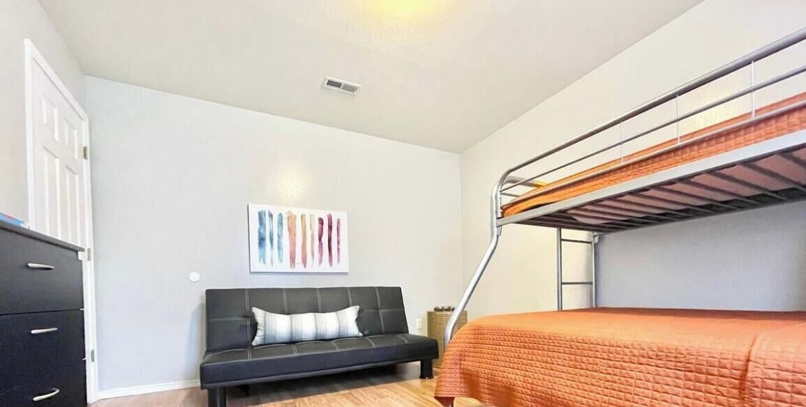Un dormitorio con una cama litera, un sofá, un aparador y una obra de arte en la pared.