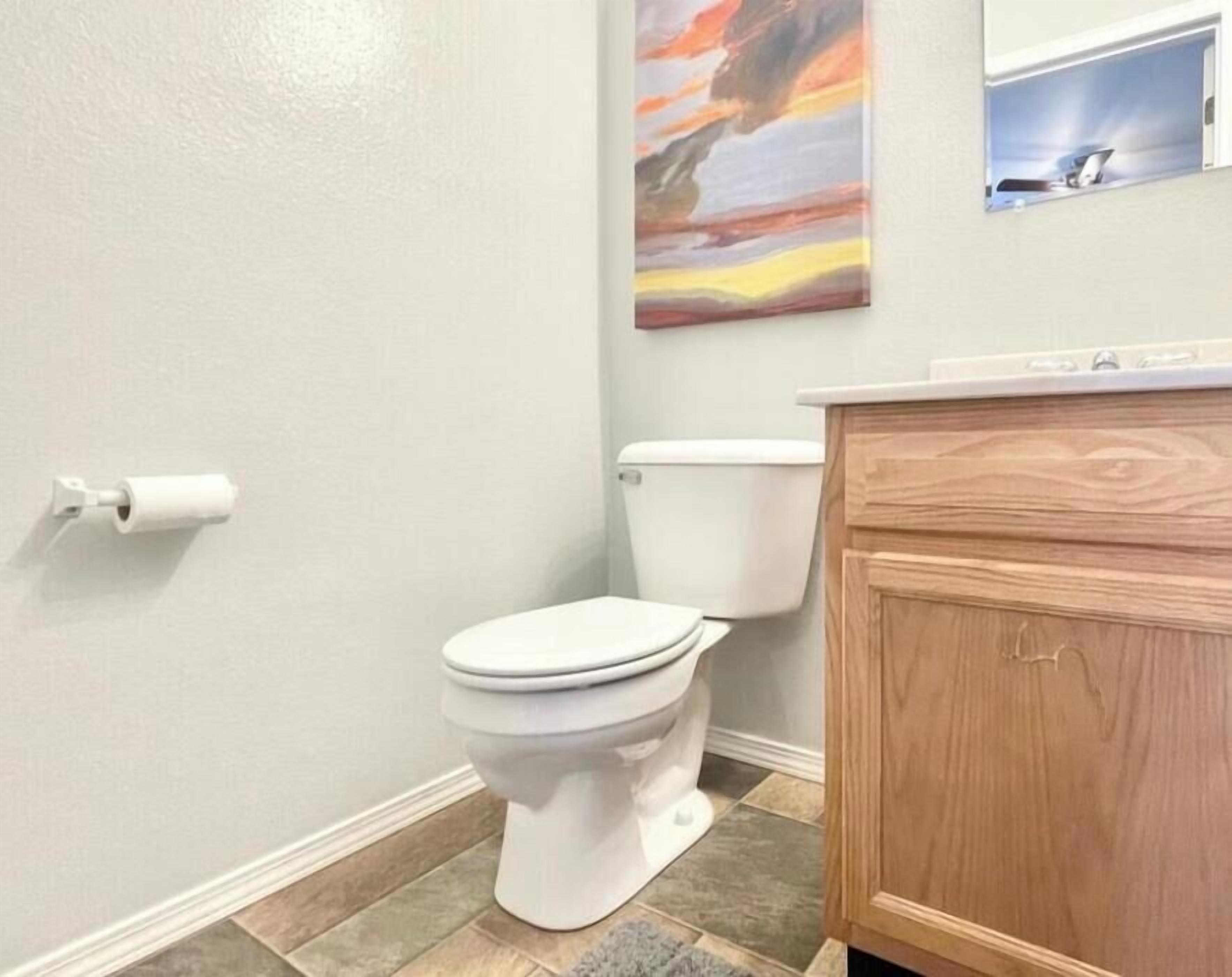 Un baño con inodoro, un armario de madera y un cuadro en la pared.