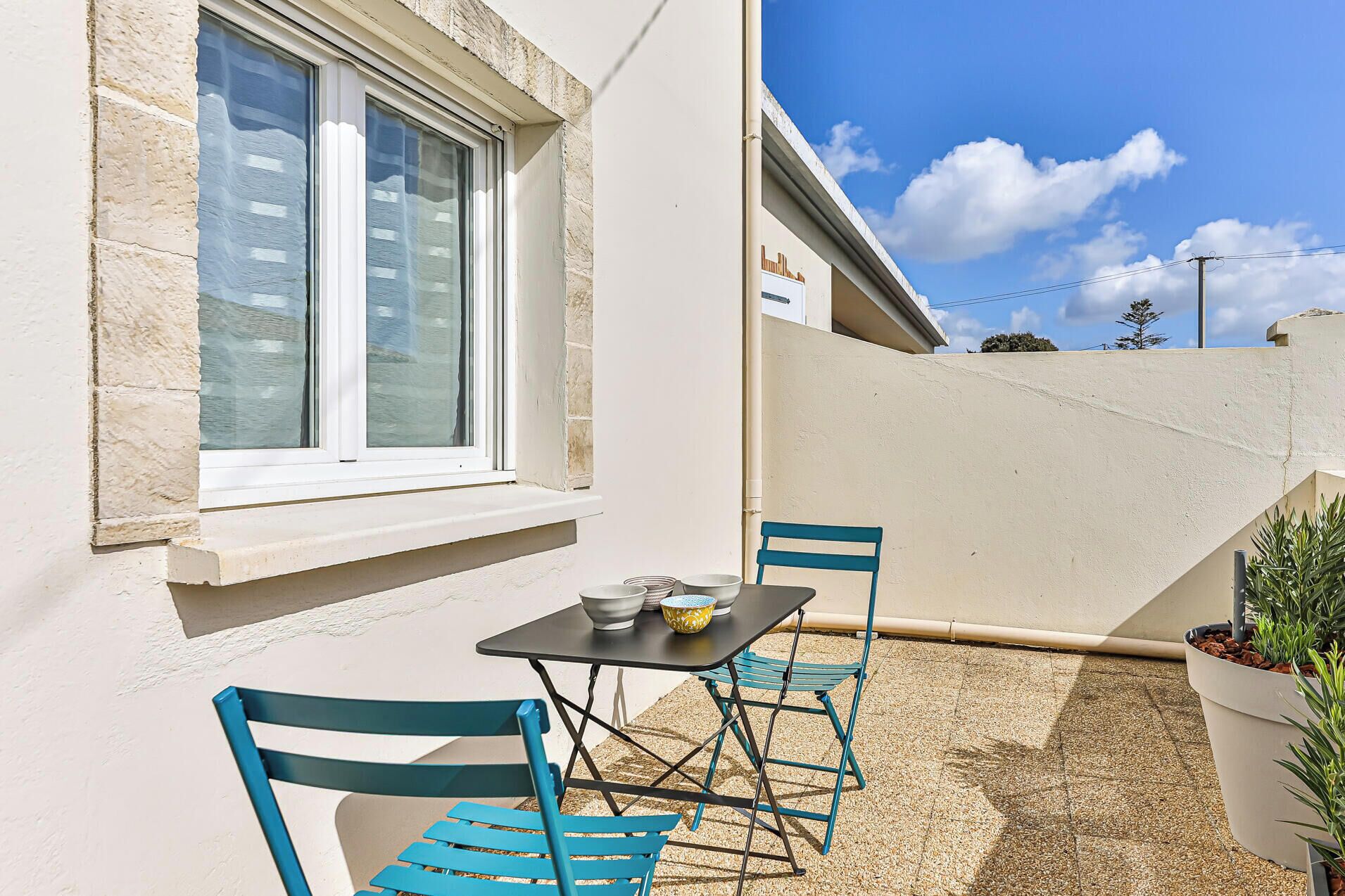 Un balcon avec une table et des chaises, une fenêtre et des plantes en pot.