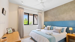 A bedroom with a bed, a nightstand, a desk, a ceiling fan, and a window with curtains. - La Balise Marina - Two Bedroom Apartment, Sleeps 4 (Rivière Noire)