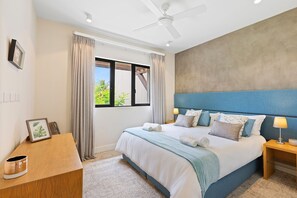 A bedroom with a bed, a nightstand, a desk, a ceiling fan, and a window with curtains.