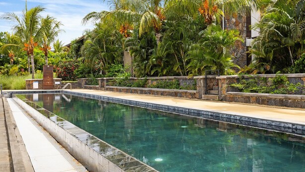 A swimming pool surrounded by tropical vegetation and stone walls. - La Balise Marina - Two Bedroom Apartment, Sleeps 4 (Rivière Noire)
