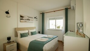 A bedroom with a bed, bedside tables, a dresser, a window with curtains, and wall art. - FLH Armação Pêra Beachside Bliss (Armação de Pêra)