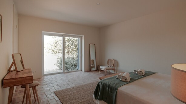 A bedroom with a bed, a desk, a chair, a mirror, and a window with a view of trees. - FLH Luz Tavira Al-Lagar I (Tavira)