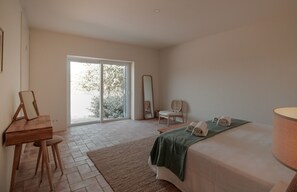 Een slaapkamer met een bed, een bureau, een stoel, een spiegel en een raam met uitzicht op bomen.