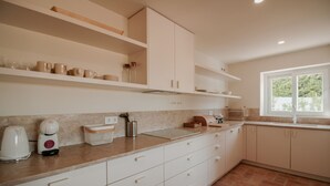 A kitchen with white cabinets, a countertop with a coffee maker, and a window with a view of greenery. - FLH Luz Tavira Al-Lagar I (Tavira)