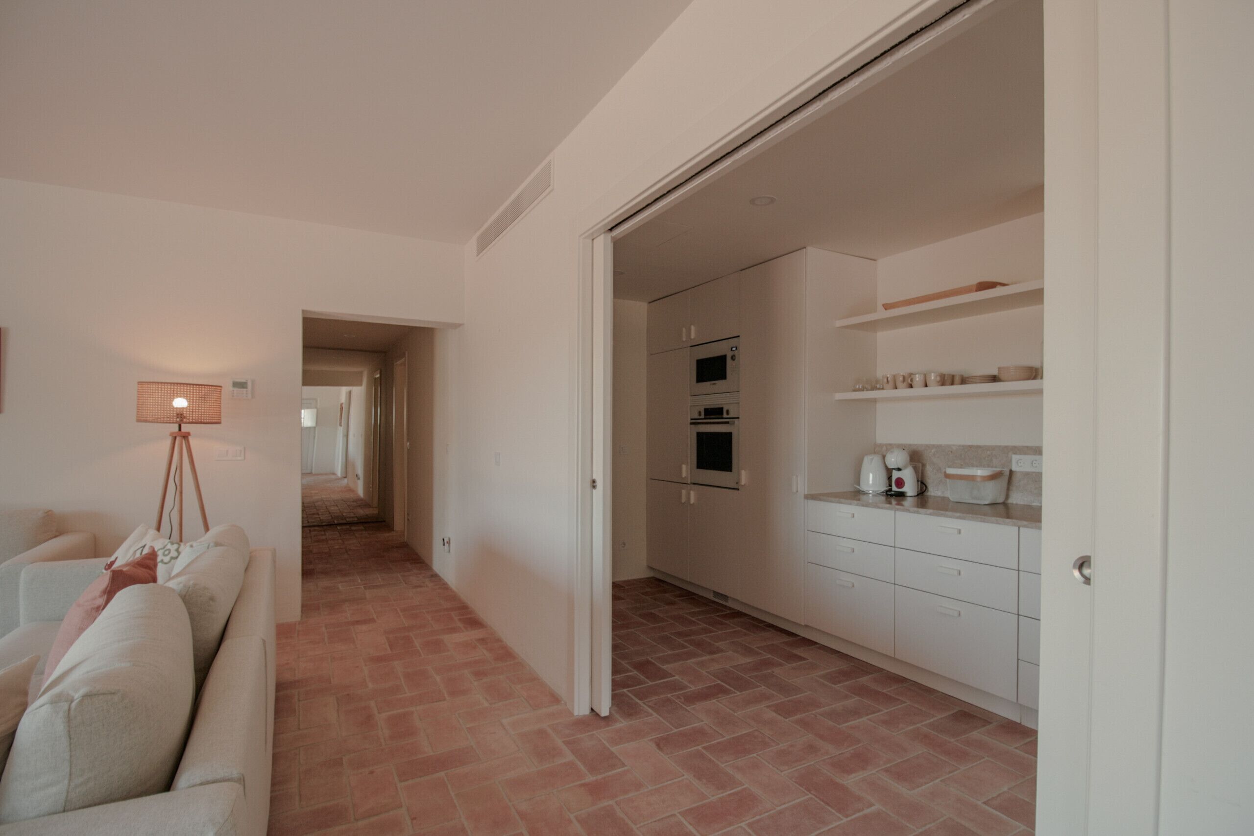 Un interior moderno con un sofá, una lámpara, una cocina con armarios y electrodomésticos, y un pasillo que lleva a otra habitación.