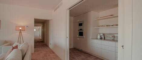Un interior moderno con un sofá, una lámpara, una cocina con armarios y electrodomésticos, y un pasillo que lleva a otra habitación.