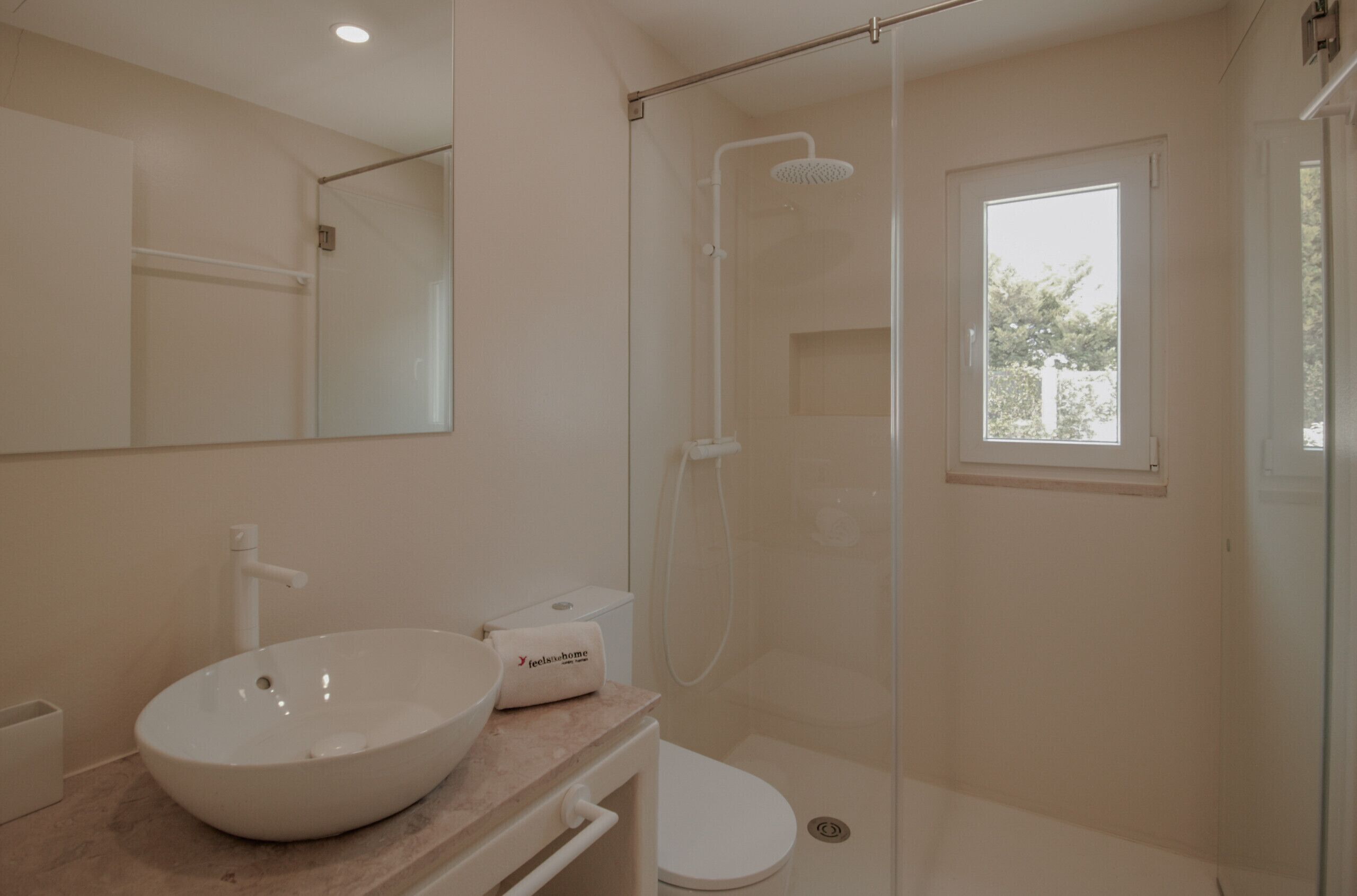 Ein Badezimmer mit einem großen, weißen Waschbecken, einer Toilette, einer Duschkabine und einem Fenster für natürliches Licht.