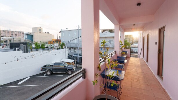 A balcony with a view of the street, a parked car, and a row of tables and chairs. - San Juan Group Stay | 16 Rooms | Sleeps 32| Parking (San Juan)