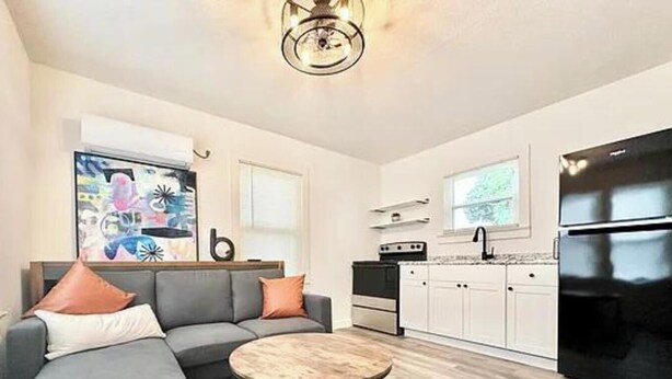 A modern living room with a grey sofa, a round coffee table, and a kitchen area with white cabinets and a black refrigerator. - Cozy 1BR Entire Unit in W. Plains, nice location! (West Plains)
