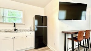 A kitchen with white cabinets, a black refrigerator, a window with blinds, and a flat-screen TV mounted on the wall. - Cozy 1BR Entire Unit in W. Plains, nice location! (West Plains)