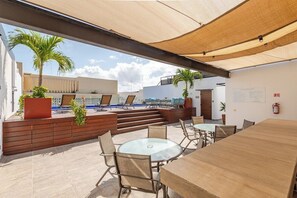 Une terrasse extérieure avec des tables et des chaises, un banc en bois et des plantes en pot.