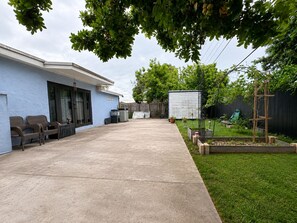 Ein Garten mit Terrasse, Stühlen, einem kleinen Gemüsegarten und einem Schuppen.