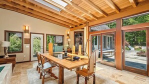 Een ruime eetruimte met een houten tafel en stoelen, grote ramen en uitzicht op de omgeving.