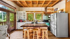 Een keuken met een houten kookeiland, barstoelen, een koelkast en uitzicht op groen.