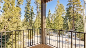 A wooden deck with a metal railing overlooking a snowy landscape with tall evergreen trees.