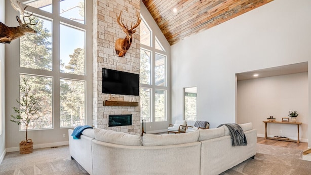 A spacious living room with a stone fireplace, a large window, and a mounted deer head.