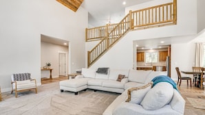 A spacious living area with a large sectional sofa, a wooden staircase, and a kitchen in the background.