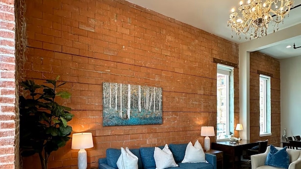 Un salon avec un mur en briques, un canapé bleu, un lustre et un tableau.