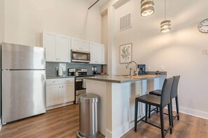 Een moderne keuken met roestvrijstalen apparatuur, witte kasten en een bar met twee stoelen.