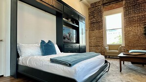 Une chambre moderne avec un grand lit, un téléviseur intégré, un lustre et un mur en briques.
