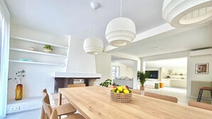 Un comedor amplio con una larga mesa de madera, luces colgantes blancas y un frutero.