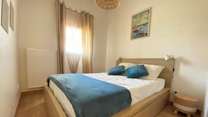 A bedroom with a wooden bed, a blue blanket, and a small round wicker side table. - Air-conditioned house in the Arcachon style with swimming pool (La Teste-de-Buch)