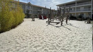 A sandy playground area with a slide and climbing structures, surrounded by multi-story buildings with balconies. - Air-conditioned house in the Arcachon style with swimming pool (La Teste-de-Buch)