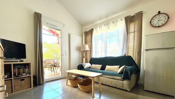 A living room with a sofa, television, table, and a clock on the wall. - Air-conditioned house in the Arcachon style with swimming pool (La Teste-de-Buch)