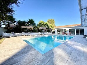 A swimming pool with lounge chairs, surrounded by a wooden deck and palm trees. - Sublime property in the heart of the Hume (Gujan-Mestras)