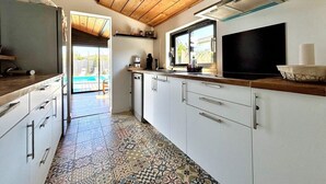 Une cuisine avec un plafond en bois, des placards blancs, un téléviseur et une fenêtre donnant sur une piscine.