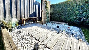 Une terrasse en bois avec une table, entourée de petits galets blancs et d’une haie.