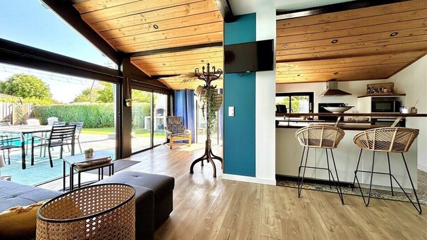 Un intérieur moderne avec un plafond en bois, un espace cuisine et un coin salon offrant une vue sur l’extérieur.