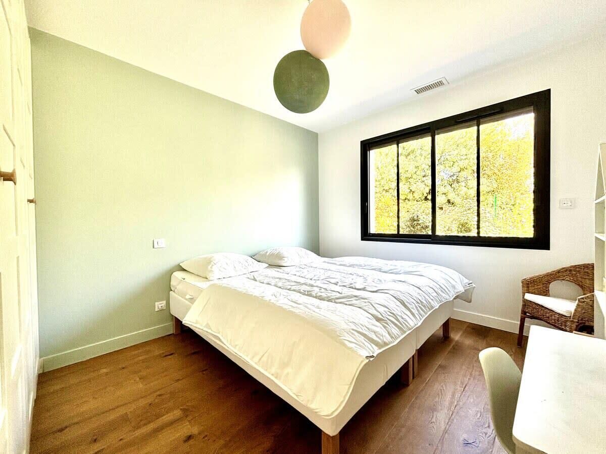 Ein Schlafzimmer mit Bett, einem Fenster mit Blick auf Bäume, einem Sessel und einem Regal.