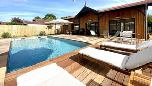 Ein Schwimmbecken mit Liegestühlen und Sonnenschirmen, ein Holzdeck und ein Gebäude mit großen Fenstern.